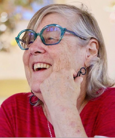 Fran Goldfarb wearing a red top and blue glasses, smiling.